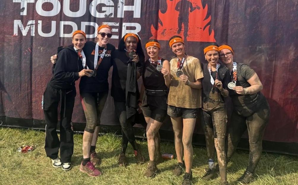 Angela Rayner and five other women, covered in mud and wearing orange headbands, pose with medals in front of a banner that reads "FINISHER TOUGH MUDDER."