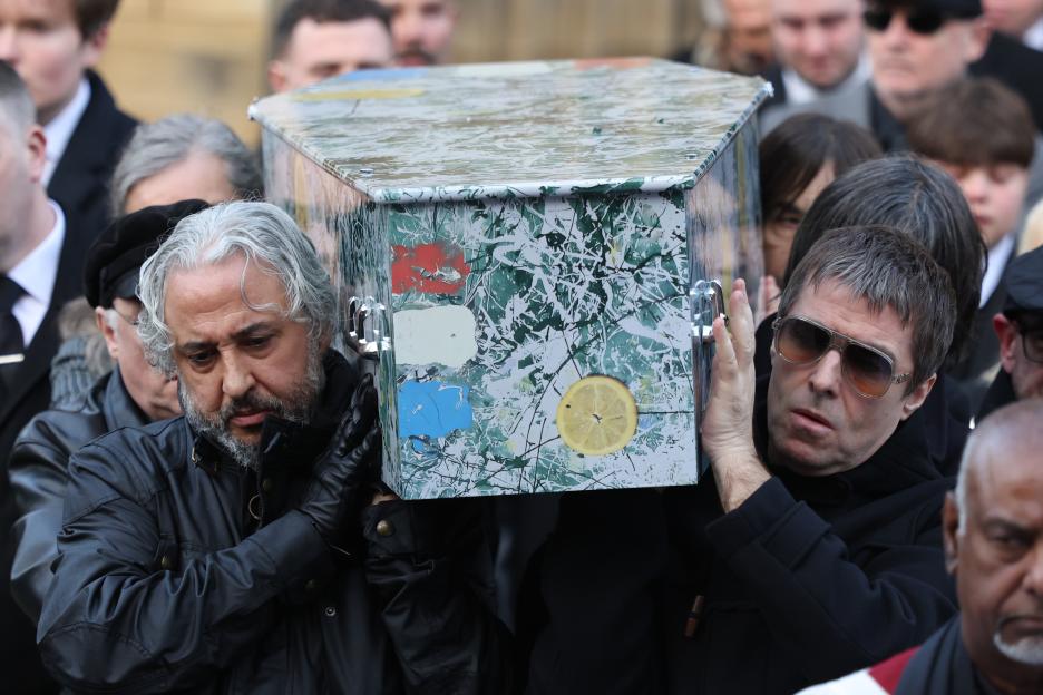 Musicians Alan Wren and Liam Gallagher carry a coffin decorated with abstract art and a lemon slice.