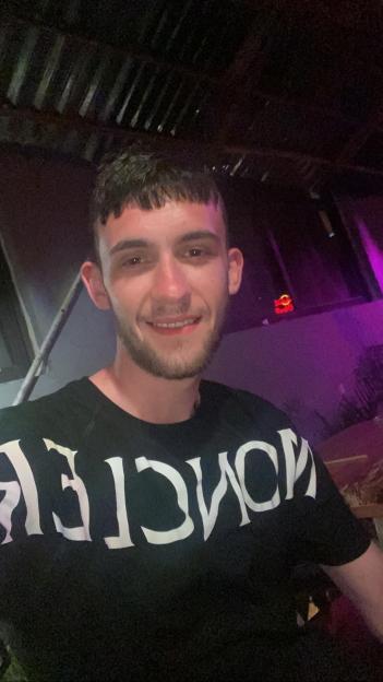 A young man with short dark hair and a beard smiling while wearing a black t-shirt.