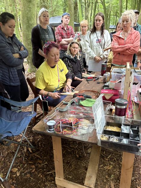 A woman demonstrates a craft at a table with art supplies to a group of people at Camp Wildfire.