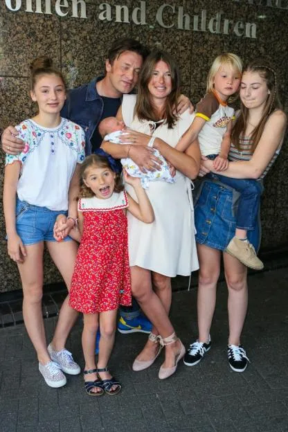 Jamie Oliver, Jools Oliver and their family pose with their new baby outside the hospital.