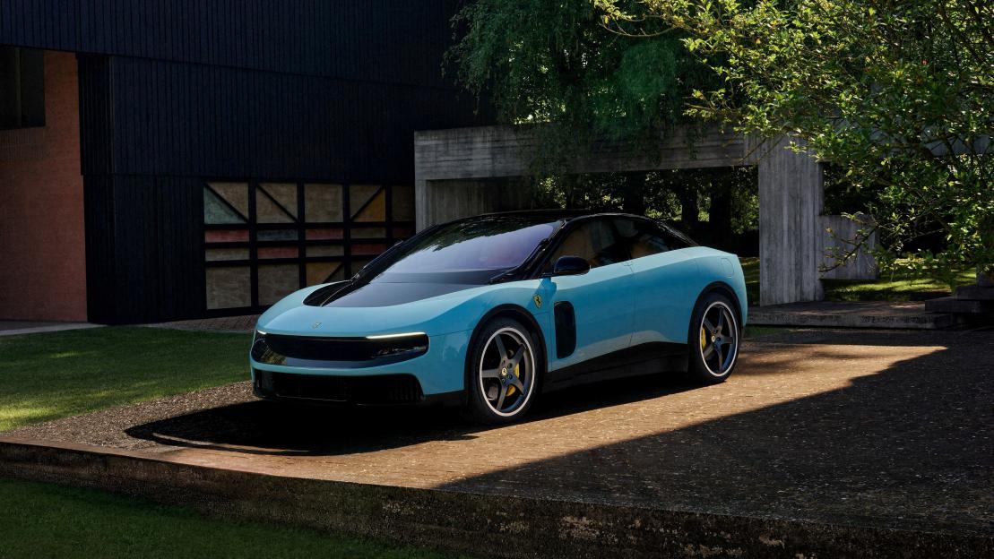 A light blue Ferrari Luce electric car parked on a concrete slab in front of a modern dark building.