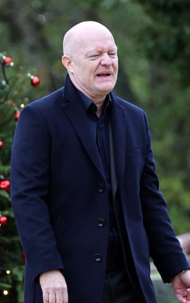 A man with a split lip and bruised face wearing a dark coat and shirt, following an argument during a christening.