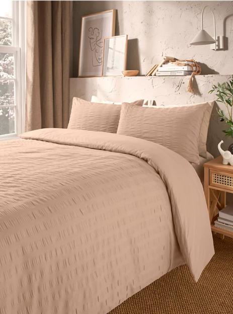 A bedroom featuring light pink bedding on a bed next to a window.