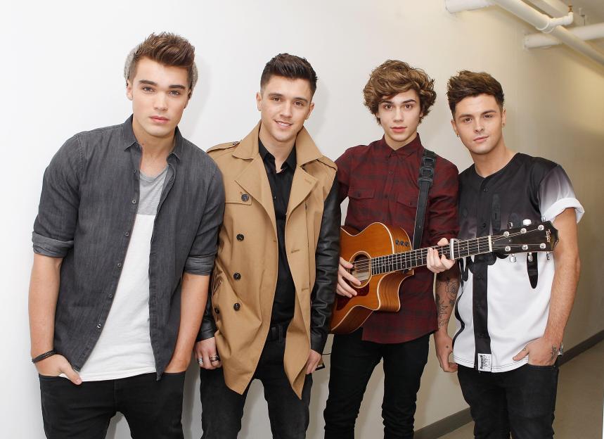 Josh Cuthbert, JJ Hamblett, George Shelley, and Jaymi Hensley of Union J posing with a guitar.