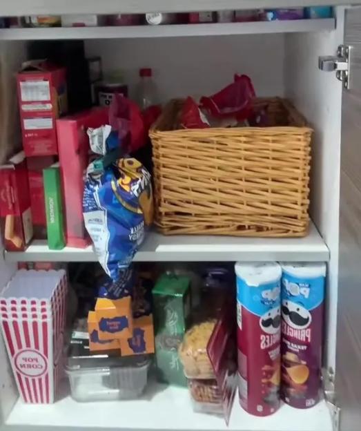 Open pantry cabinet filled with snacks including Pringles, popcorn containers, and chips.