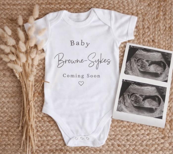 White baby onesie with "Baby Browne-Sykes Coming Soon" printed on it, next to two ultrasound scans.