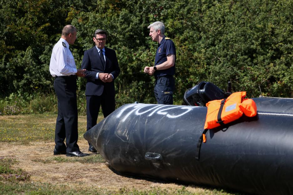 Britain's Prime Minister Andy Burnham speaks with John Craig and Duncan Capps near a recovered small boat.