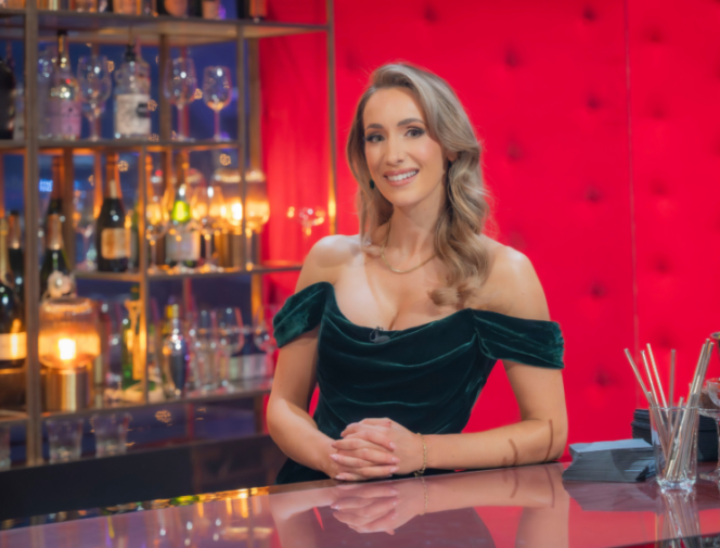 Amy Irons smiling behind a bar counter, wearing an off-the-shoulder green velvet dress.