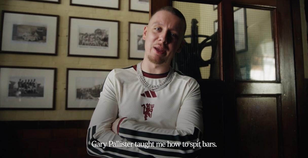 A man with a goatee, wearing a white Manchester United jersey and a diamond chain, talks to the camera.