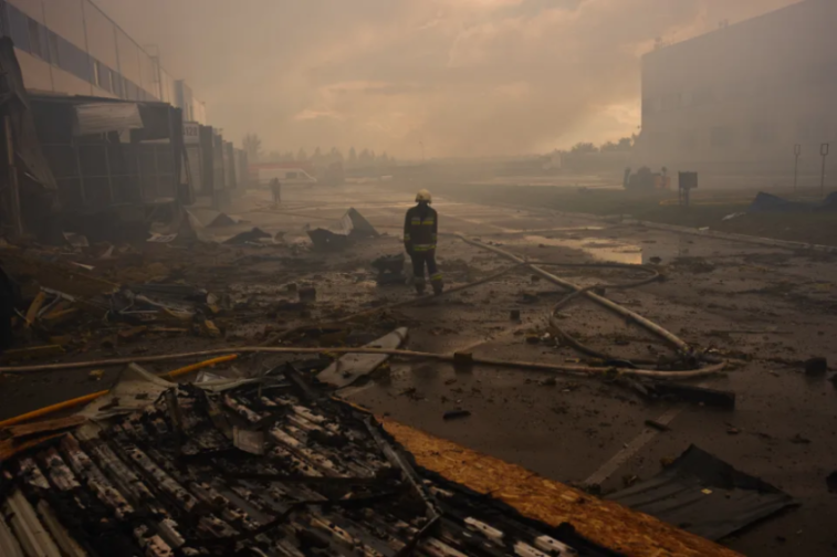 A firefighter stands amidst the rubble and smoke of a destroyed commercial area.