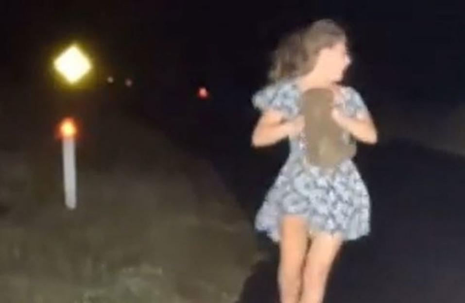 A young girl in a dress holding a large animal by its legs on a dark road at night.