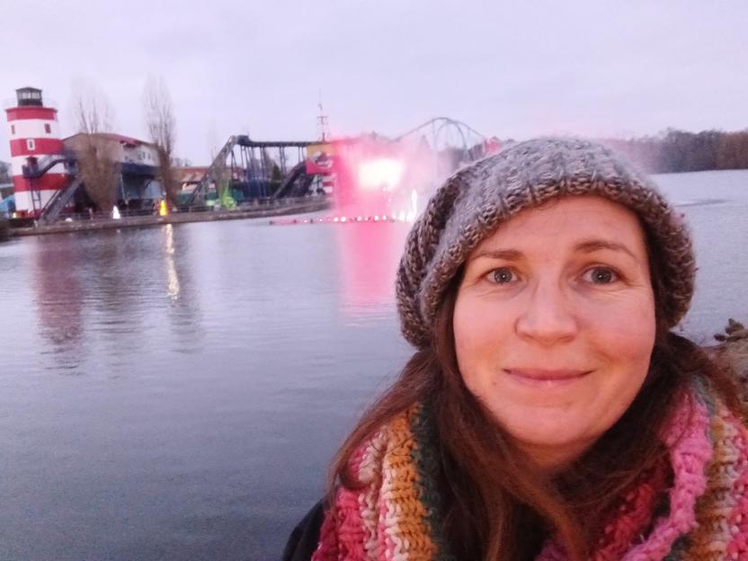 A woman smiling at Drayton Manor with a light show on the lake in the background.