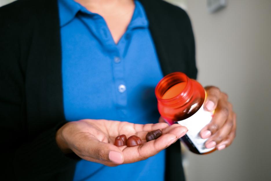 Person holding multivitamins in their palm and an open bottle.