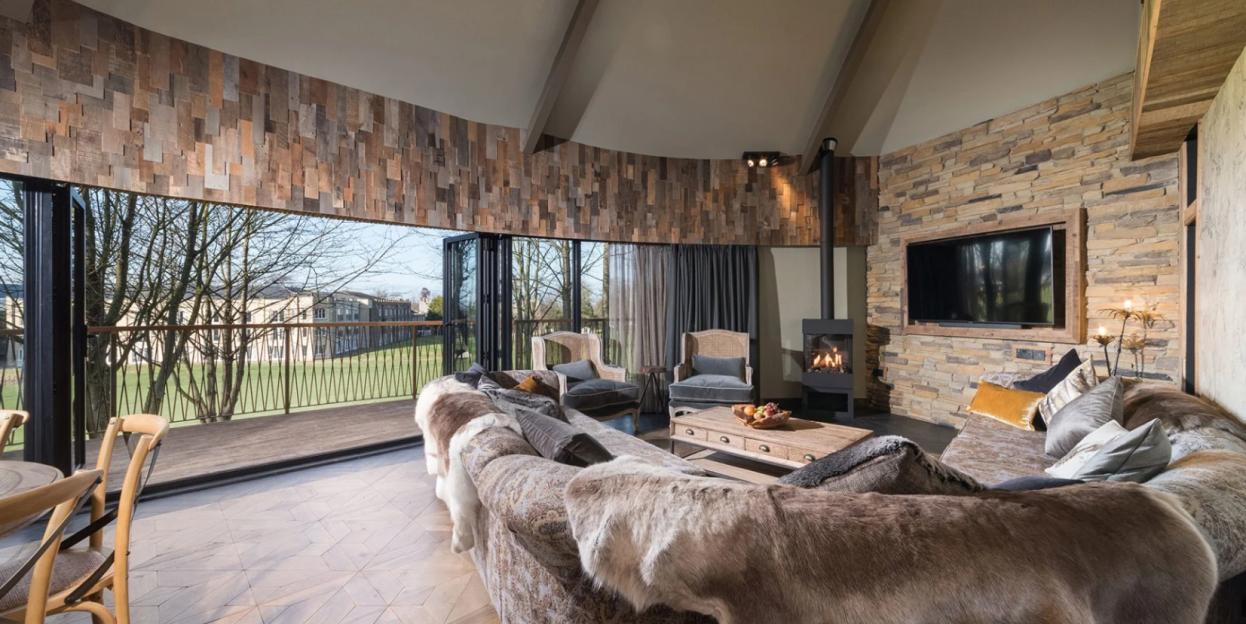 The Ramside Hall Hotel, Golf & Spa features a spacious living area with a large balcony overlooking the golf course, a stone-faced wall with a TV, a fireplace, and a sofa covered in faux fur.