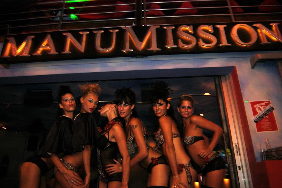 Six women in skimpy outfits posing outside "Manumission" nightclub.