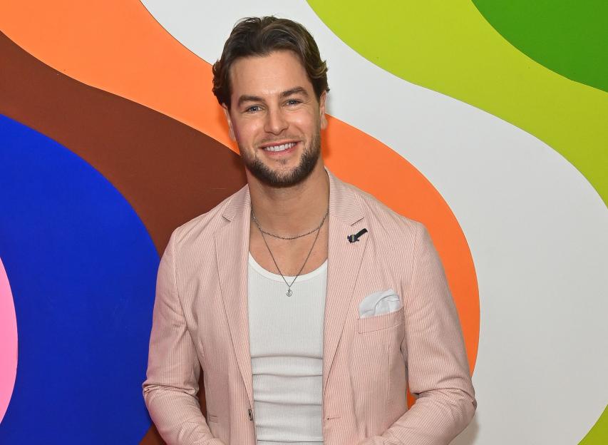 Chris Hughes attends the Universal Music BRIT Awards after-party wearing a pink blazer, white ribbed tank top, navy pants, and white sneakers.