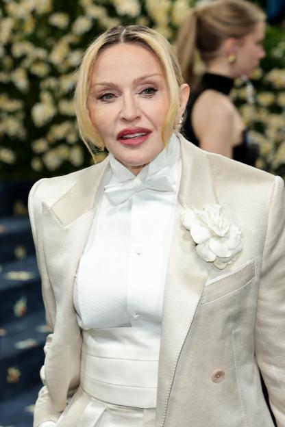 Madonna attends the 2025 Met Gala in a cream suit with a white bow tie and a white floral brooch.