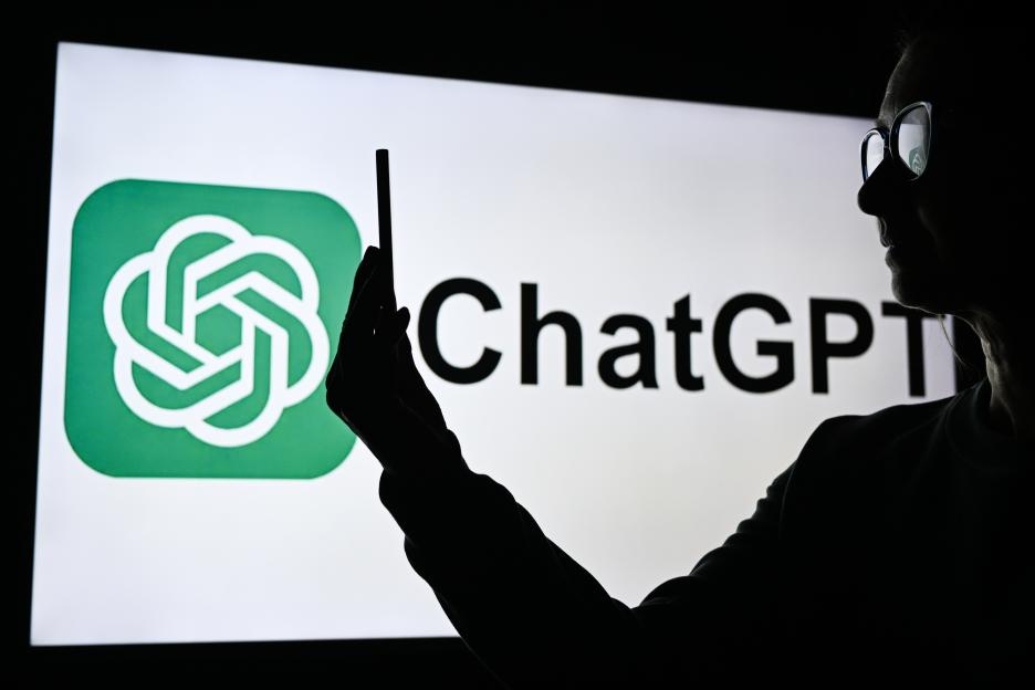 Silhouette of a woman holding a phone in front of a screen displaying the ChatGPT logo.