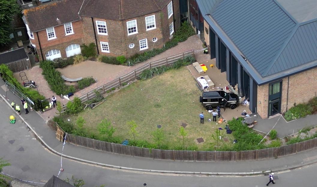 Aerial view of a black Land Rover Defender crashed into a school building.