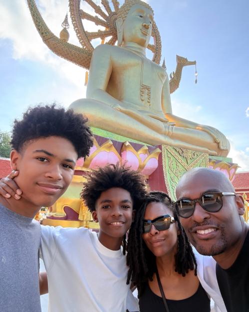Paul C Brunson and his family pose for a selfie in front of a large golden Buddha statue.