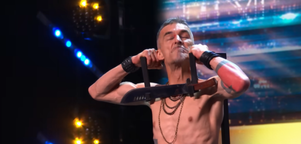 A man holding a sword pressed against his neck on stage.