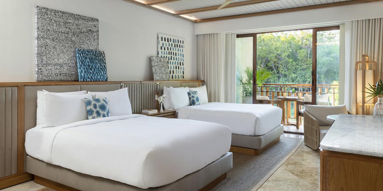A hotel room at Fairmont Mayakoba with two beds and a balcony overlooking a lush green landscape.