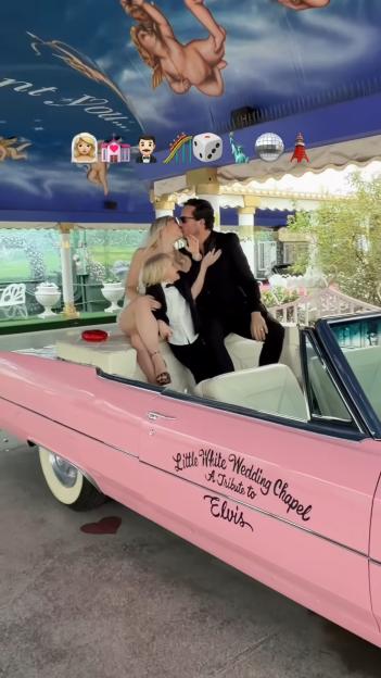A newlywed couple kisses in a pink Cadillac at a Vegas wedding chapel, with a child between them.