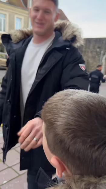 A man in a black coat and fur-lined hood smiles while a child, seen from behind, looks towards him.