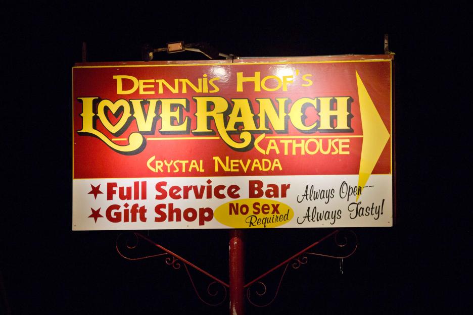 A red and yellow sign for "Dennis Hof's Love Ranch Cathouse" in Crystal, Nevada, advertising "Full Service Bar," "Gift Shop," and "No Sex Required."