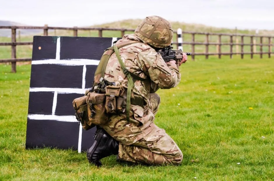 A British Army soldier kneels on a firing range with an assault rifle.