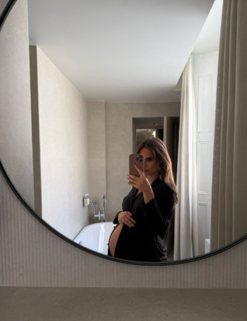 A pregnant woman in a black shirt taking a mirror selfie.