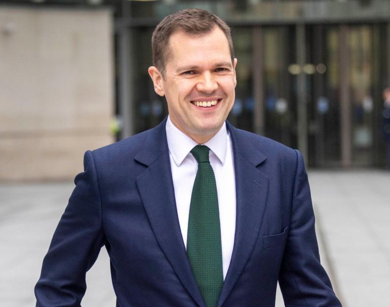 Robert Jenrick, Chancellor for Reform, smiling while walking past an autograph hunter holding a picture of him.
