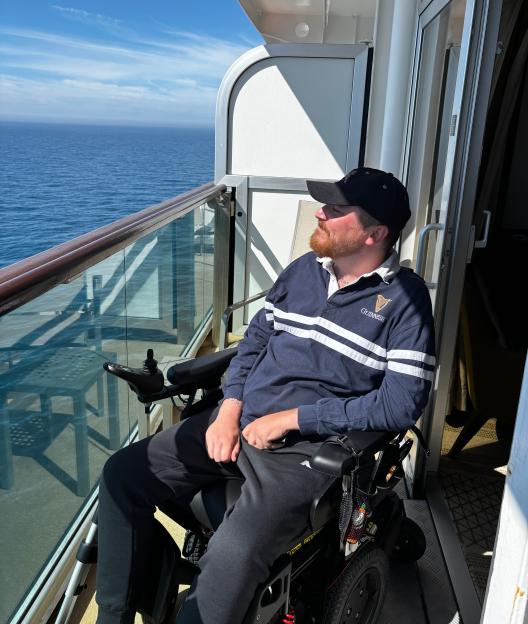 A man in a wheelchair on a balcony overlooking the ocean.