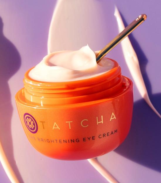 Tatcha The Brightening Eye Cream in an orange jar with a small golden spoon in the cream.