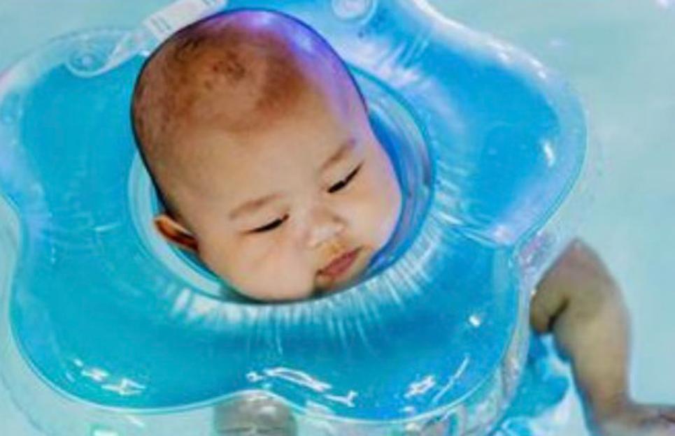 A baby with a blue inflatable neck float around its neck, floating in water.