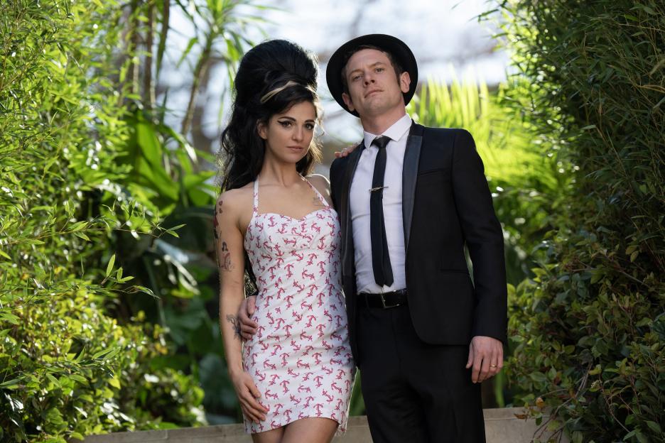 Woman dressed as Amy Winehouse and a man in a suit and hat posing outdoors.