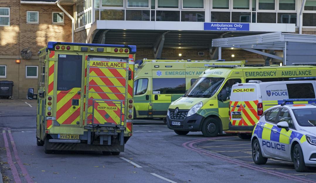 Emergency vehicles, including several ambulances and a police car, parked outside a hospital building with an "Ambulances Only" sign.