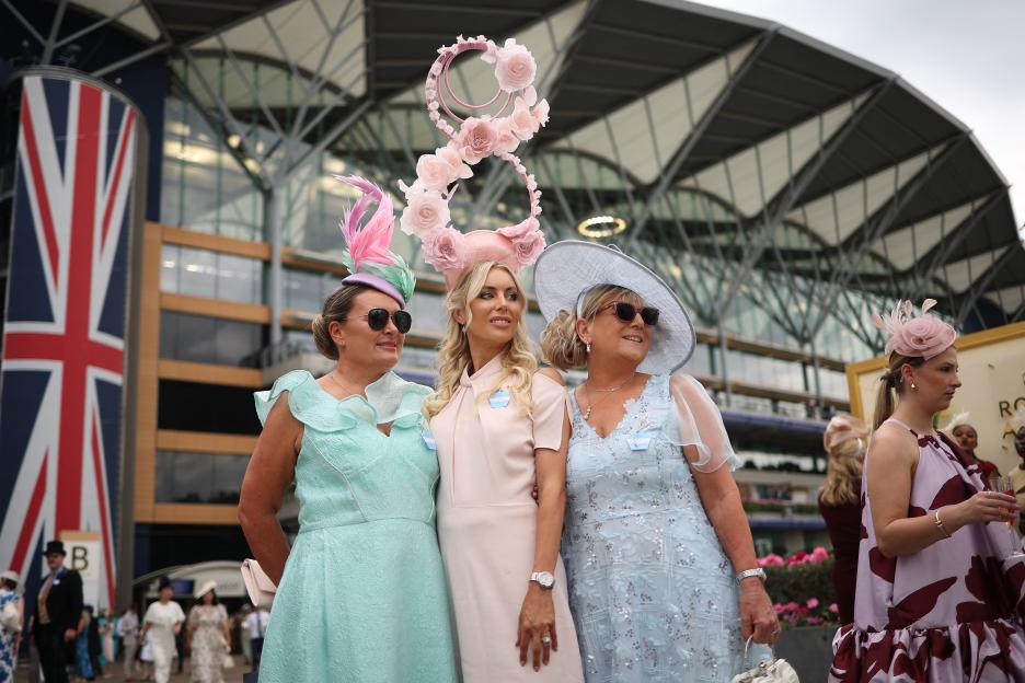 Three women in elegant dresses and hats at a horse race.