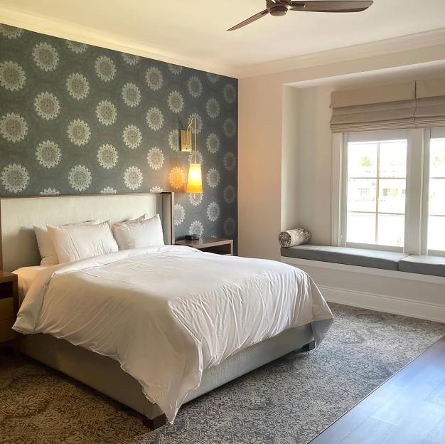 A hotel room at The Inn at Meadowbrook with a large bed, decorative wallpaper, and a window bench.