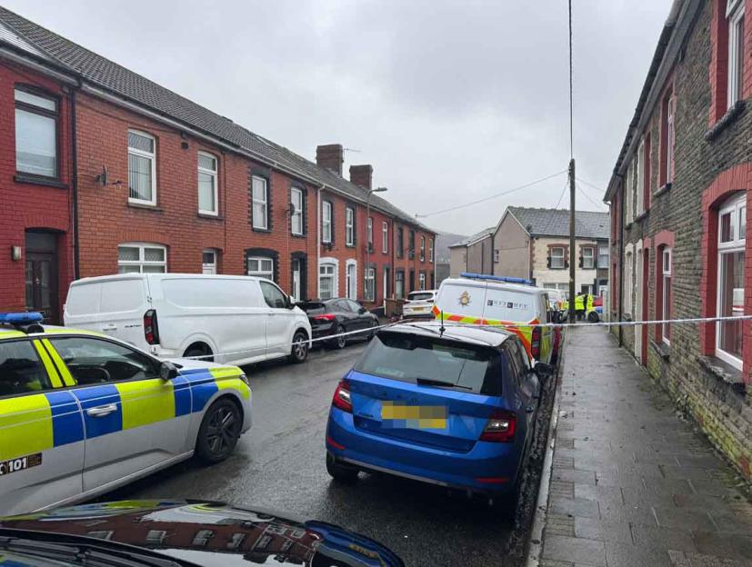 Police vehicles and crime scene tape on a street lined with residential buildings, indicating a police investigation.