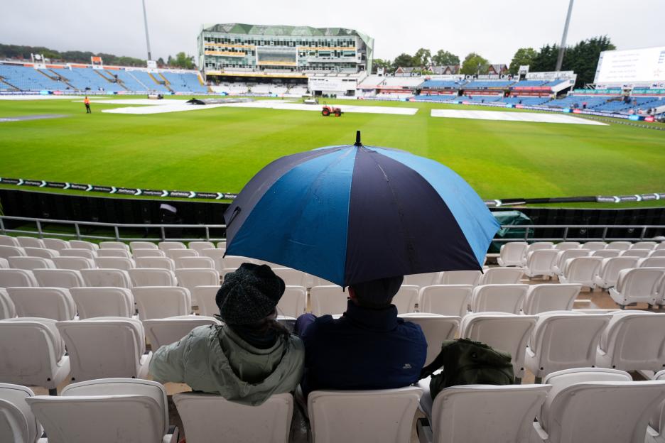 Spectators sheltering from the rain under an umbrella at Headingley cricket ground.