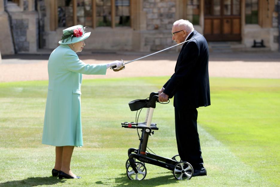 Queen Elizabeth II bestows a knighthood upon Captain Tom Moore, who uses a walker, at Windsor Castle.