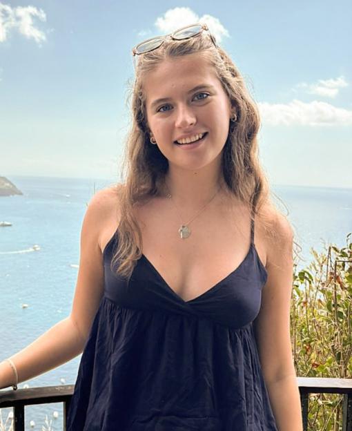 Jessica Lyons standing on a balcony overlooking a bay with many boats, with mountains in the background.
