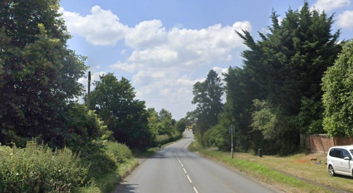 A winding road lined with trees under a blue sky with white clouds.