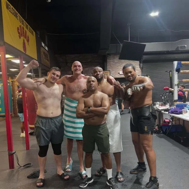 Five shirtless men posing in a boxing gym, with Tyson Fury standing in the back row wearing a striped towel.