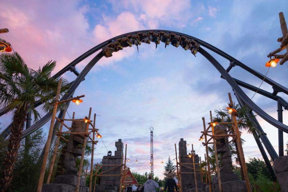 A roller coaster looping upside down against a pink and blue sunset sky at Walibi Rhone Alpes theme park.