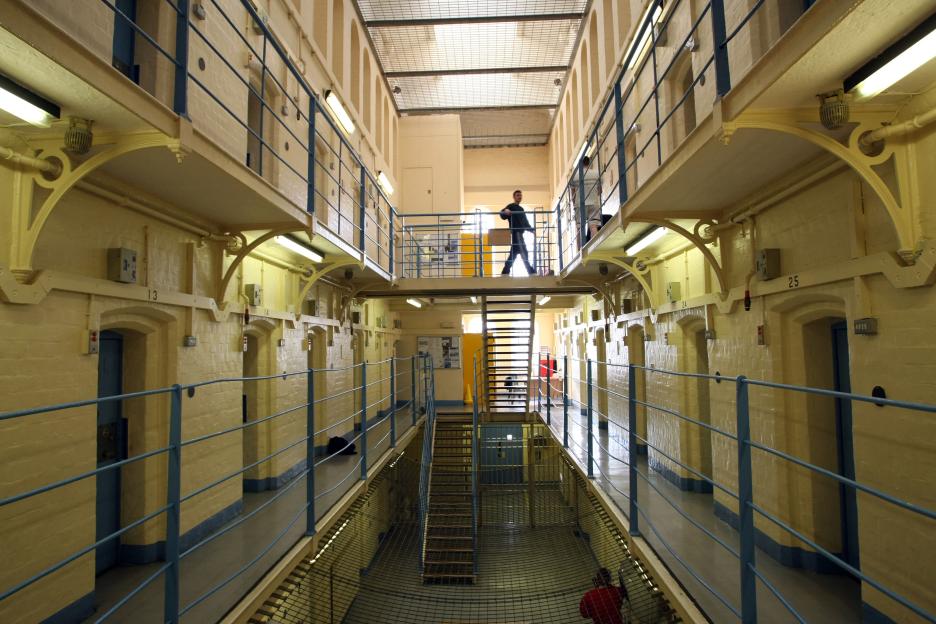 Interior of a prison hall with multiple levels of cells, a man walking on the upper level.
