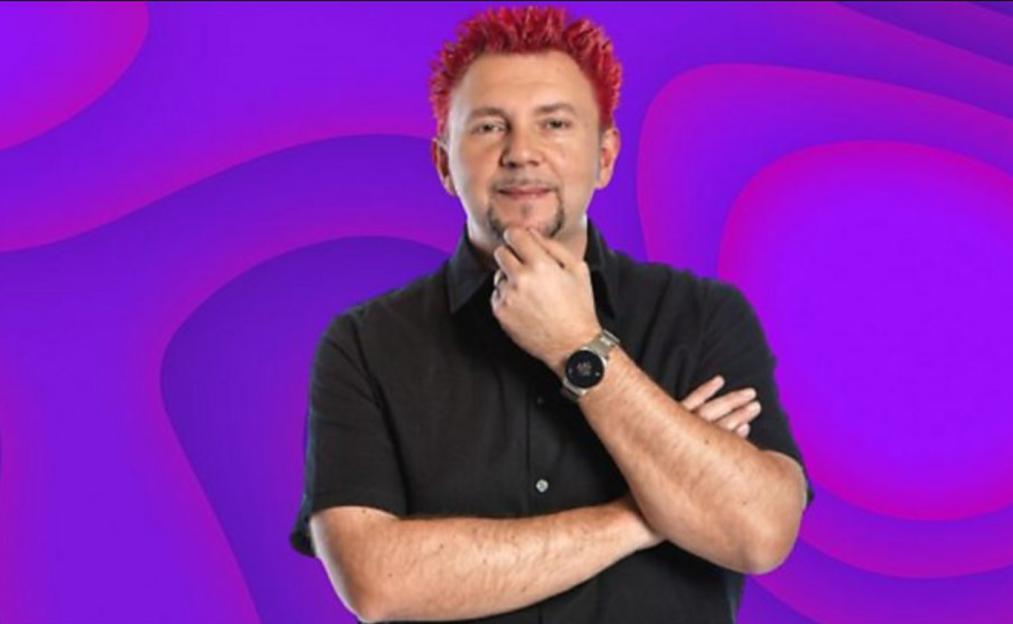 Dave Llewellyn, a man with red hair, a goatee, and a black shirt, is standing with his arms crossed and one hand on his chin.