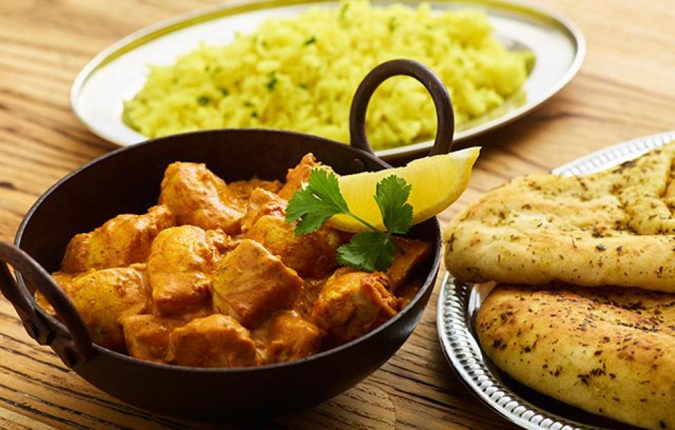 Chicken curry in a bowl with rice and naan bread on the side.